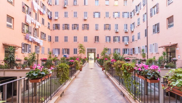 Un immeuble résidentiel à plusieurs étages, doté de balcons, de plantes en pot et d’un couloir central.