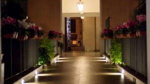 Vue nocturne de l’entrée d’un bâtiment, avec un luminaire central et des plantes en pot de chaque côté.