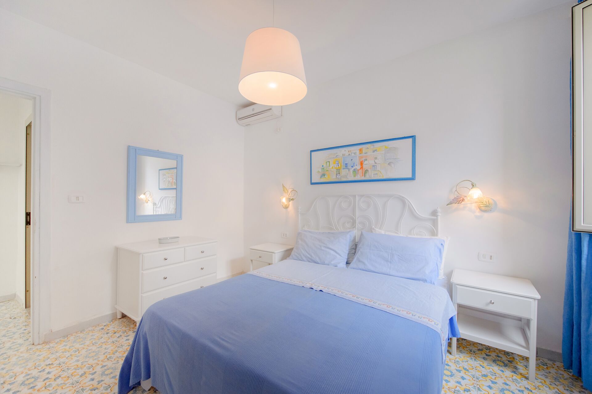 Ein Schlafzimmer mit einem Bett, Nachttischen, einem Spiegel und Wandbildern.