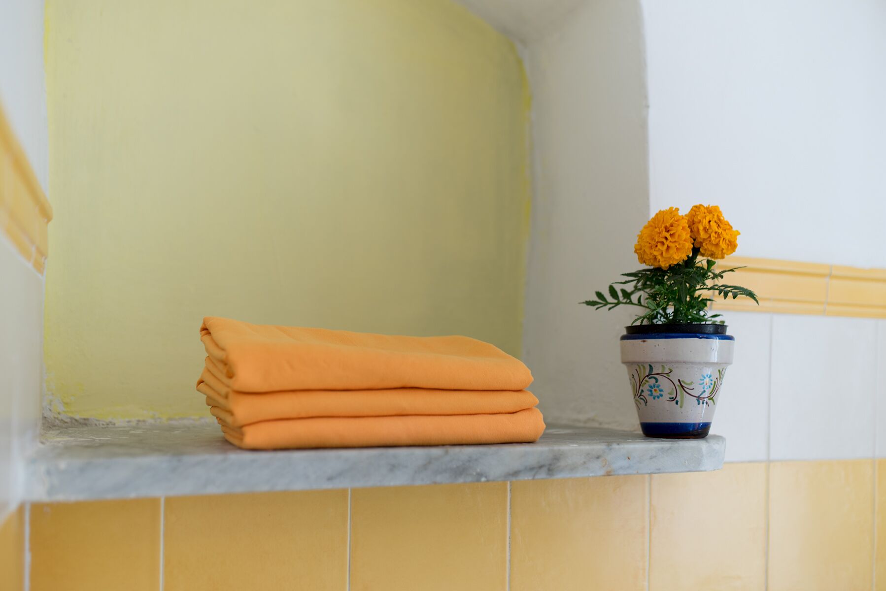 Ein Badezimmer mit gelber Wand, einer Marmorarbeitsplatte und einem Blumentopf mit gelben Blüten.