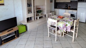Un espace de vie compact comprenant un téléviseur, un coin salon, une kitchenette et des rangements.