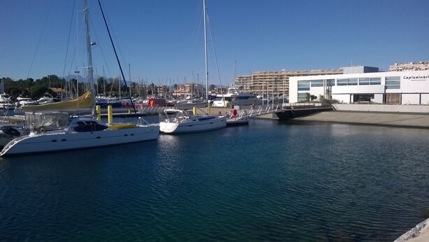 Un port de plaisance où sont amarrés plusieurs yachts, un bâtiment doté de grandes fenêtres et un ciel d’un bleu limpide.