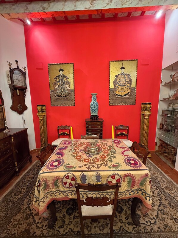 Une salle à manger avec un mur rouge, deux tableaux encadrés, un grand vase et une horloge.