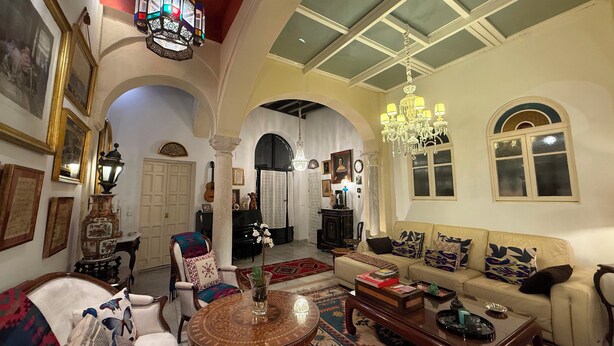 A spacious living room with a high ceiling, ornate chandeliers, and a large window.