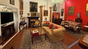 A traditional living room with a fireplace, a sofa, a television, and various framed artworks on the walls.