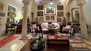 A spacious lobby with high ceilings, arched columns, a chandelier, and a central seating area with a coffee table.
