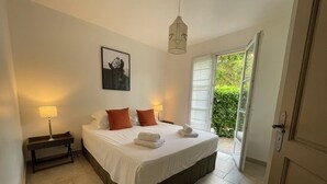A bedroom with a bed, pillows, a bedside table, a lamp, and a door leading to a balcony.
