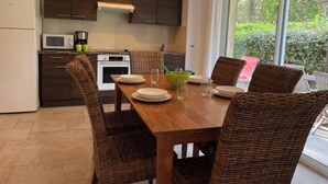A modern kitchen with dark wooden cabinets, a white refrigerator, a microwave, and a stove. There is a dining table with four wicker chairs and a green bowl.