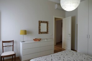 A bedroom with a bed, a dresser, a chair, a lamp, a mirror, and an open door leading to another room.