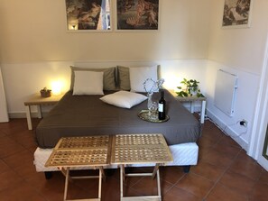 Relax in a serene bedroom with a large bed, a small wooden table, and a potted plant.