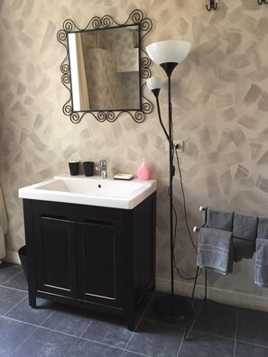 Bathroom features a vanity with a countertop and mirror, a floor lamp, and a towel rack.