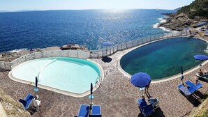 Un espace piscine comprenant deux bassins distincts, une terrasse en pierre et une vue sur la mer.