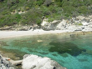 Paesaggio costiero con acque turchesi limpide, costa rocciosa e vegetazione lussureggiante.