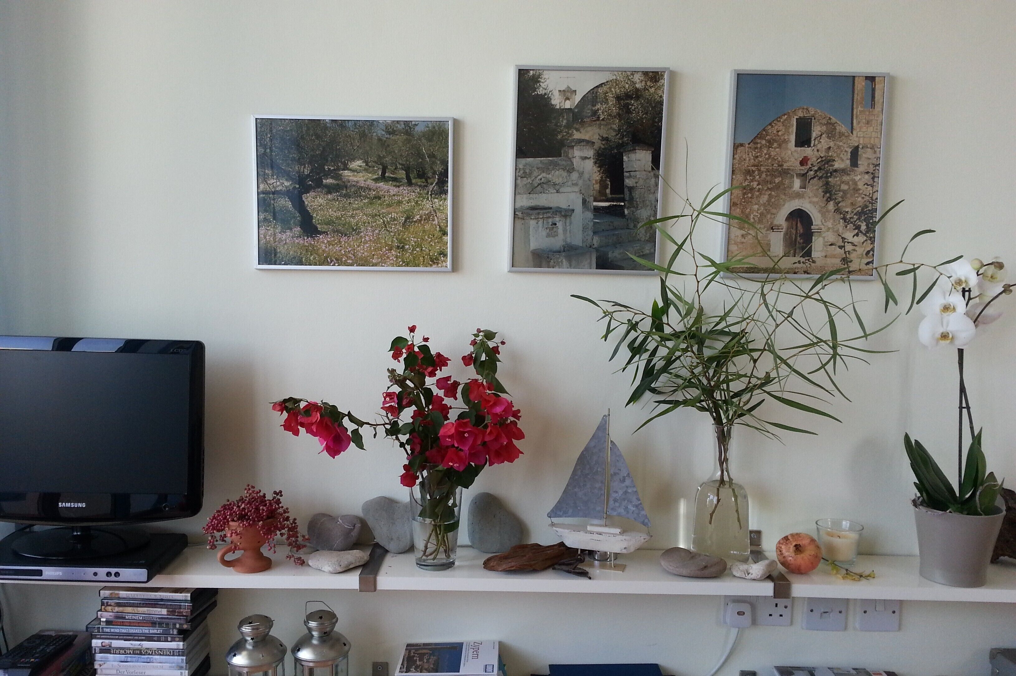 Une pièce avec un téléviseur, une étagère ornée d’objets décoratifs et des tableaux encadrés accrochés au mur.