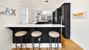 A modern kitchen with a white countertop, three stools, and a black cabinet. - Time Out - Destiny East Lux Villa. Pool, Hot Tub, 2 Golf Carts 🛺, 6BR (Destin)