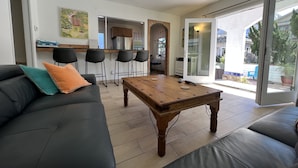 A modern living room with a sofa, a coffee table, and a kitchen area visible through an open door. -  ☀️Sunny Courtside House, 🏖STEPS TO OCEAN OR BAY, Bikes! South Mission BeachSD (San Diego)