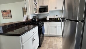 A modern kitchen with white cabinets, a stainless steel refrigerator, a microwave, and a stove. -  ☀️Sunny Courtside House, 🏖STEPS TO OCEAN OR BAY, Bikes! South Mission BeachSD (San Diego)