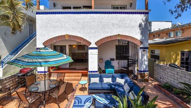 A patio with a dining table, chairs, a striped umbrella, a blue sofa, and a patterned rug. -  ☀️Sunny Courtside House, 🏖STEPS TO OCEAN OR BAY, Bikes! South Mission BeachSD (San Diego)