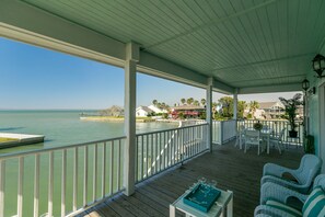 A covered deck with a view of the water, white railings, and outdoor furniture.