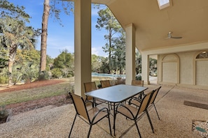 Un patio exterior con una mesa y sillas, rodeado de árboles y una piscina.