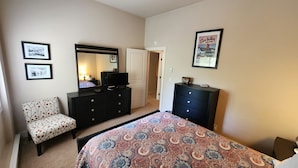 Un dormitorio con cama, cómoda, silla, espejo y dos cuadros en la pared.