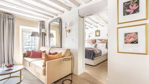 Ein gemütliches Schlafzimmer mit einer Couch, einem Bett und einem großen Spiegel. An den Wänden hängen Bilderrahmen und das Fenster ist mit Vorhängen versehen.