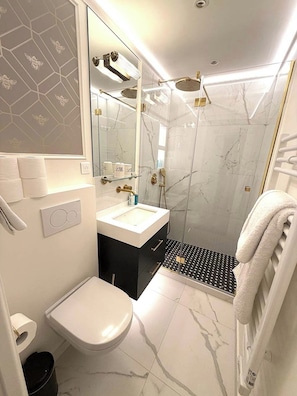 Uma casa de banho moderna com sanita, lavatório, chuveiro e área de duche com divisória de vidro.