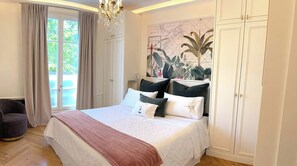 A bedroom with a large bed, a chandelier, a map on the wall, and a view through the window.