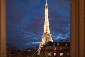 A Torre Eiffel à noite, iluminada, vista de um edifício com janelas.