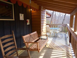 A wooden deck with a bench and chairs, a table, and a view of trees.