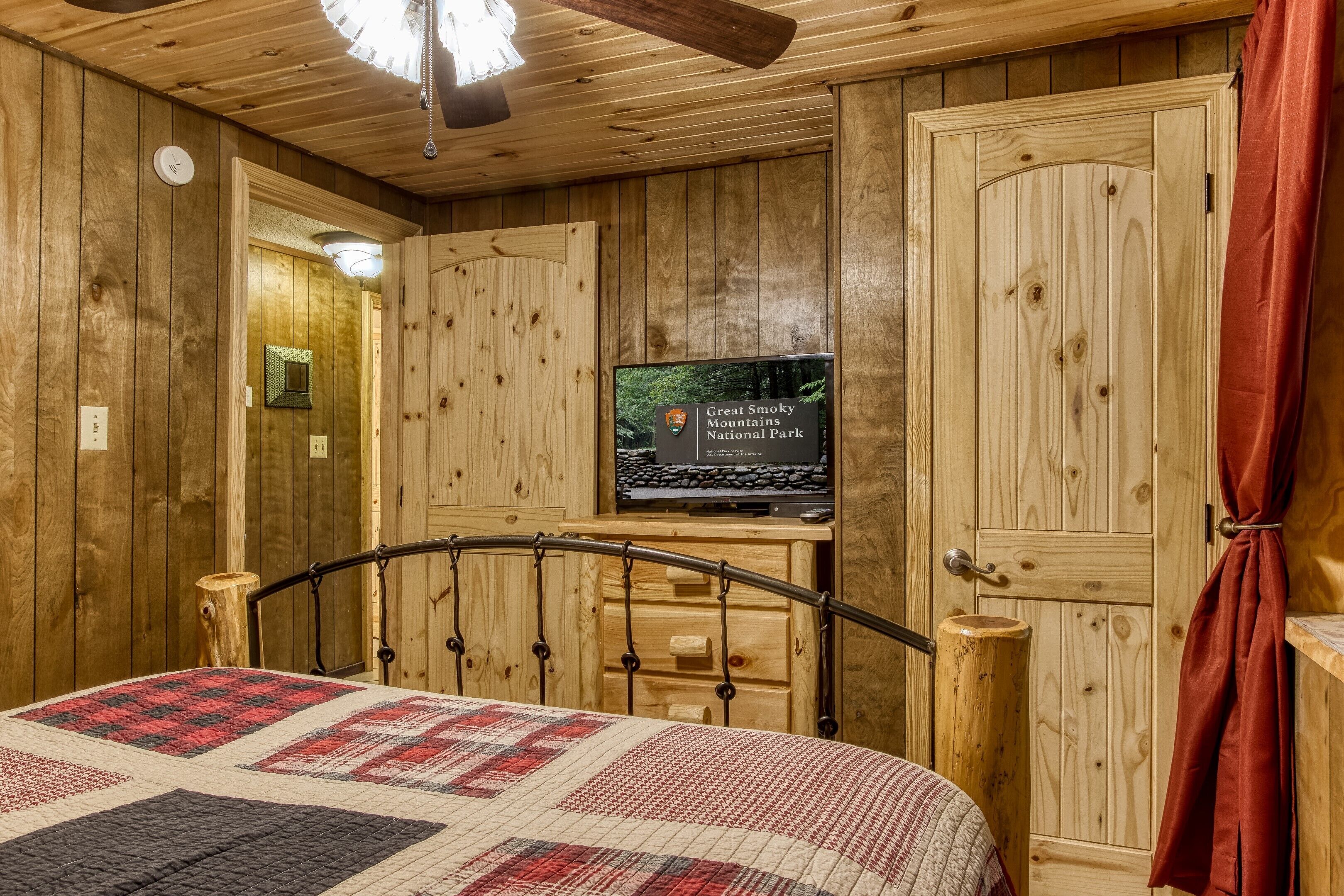 Une pièce de style cabane en bois, avec un lit, un téléviseur fixé sur un meuble en bois et une porte sur laquelle est apposée une pancarte indiquant qu’il s’agit d’un parc national.