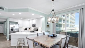Une cuisine moderne avec des meubles blancs, un îlot central et un coin repas comprenant une table et des chaises en bois.