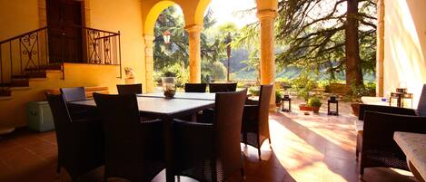 A covered patio with a dining table and chairs, surrounded by arches and potted plants.
