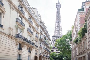 Une vue de rue avec la Tour Eiffel en arrière-plan, encadrée par des bâtiments représentatifs de l’architecture classique européenne.