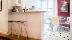Une cuisine moderne avec un coin bar, des meubles blancs et un espace repas agrémenté d’un mur d’accent rouge.