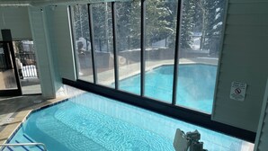 A clear indoor swimming pool with a view of a snowy landscape through large windows. - Ski-In, Ski-Out, Corner Unit. Sleeps 4. Hot Tubs, Pool, 65" OLED TV. Near Base (Winter Park)