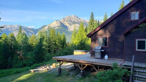 Una cabaña con terraza, una parrilla y vistas a las montañas.