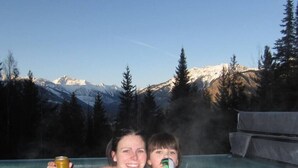Dos personas en un jacuzzi con un paisaje montañoso de fondo.