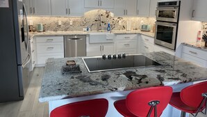 A modern kitchen with white cabinets, a granite countertop, stainless steel appliances, and red bar stools. - Kid Friendly with Breathtaking Views on 10 Acres (Sonoma)