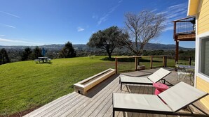 A wooden deck with lounge chairs and a table, overlooking a grassy yard and a scenic view of hills and trees. - Kid Friendly with Breathtaking Views on 10 Acres (Sonoma)