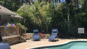A swimming pool with two lounge chairs and a wooden deck with a colorful ball.