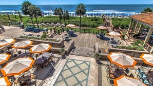 A rooftop terrace with outdoor seating, a wooden deck, and a view of the beach and ocean.