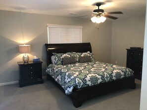 A bedroom with a bed, a nightstand, a dresser, a ceiling fan, and a window with blinds. - Celebrate at the Beach Thanksgiving! Private Pool and Free Bikes! (Hilton Head Island)