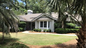 A single-story house with a front porch, surrounded by a well-maintained lawn and various shrubs.