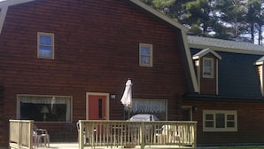 A wooden building with a porch, a red door, and a covered area with chairs.
