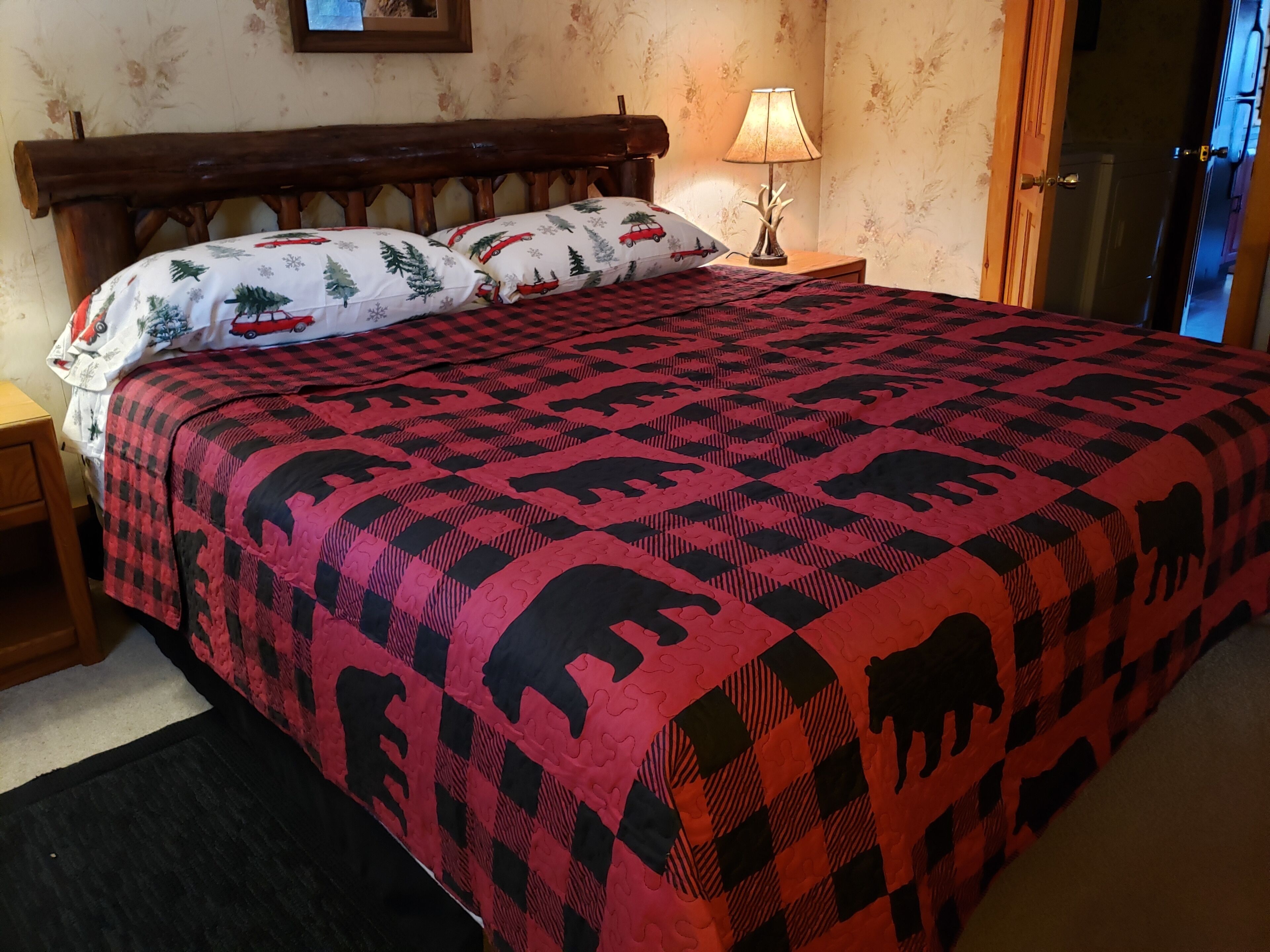 A bed with a red and black checkered bedspread featuring elephant patterns, flanked by two pillows with a red car and tree design.