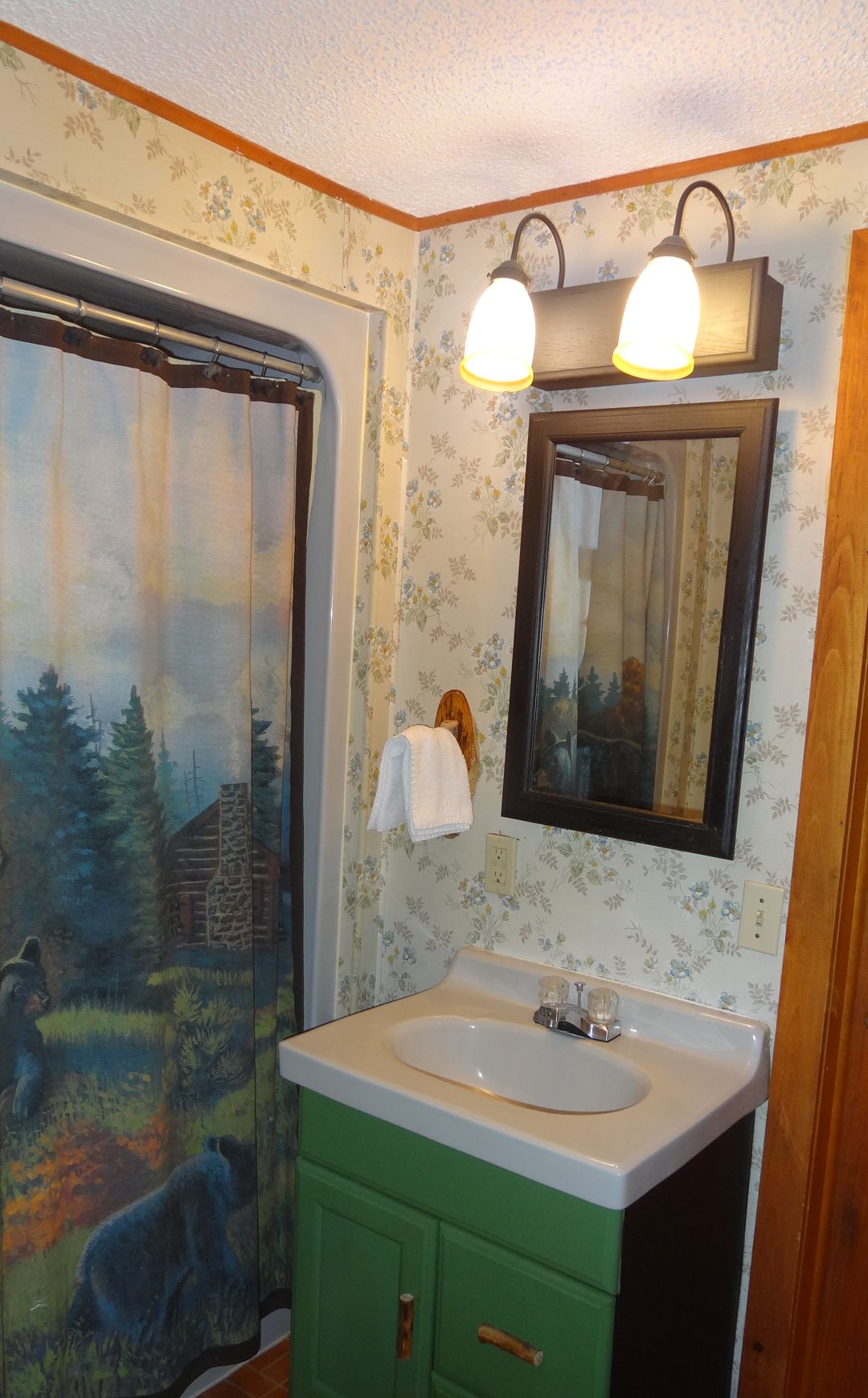 A bathroom with a green vanity, a white sink, a mirror, and a shower curtain depicting a forest scene.