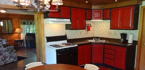 Enjoy meals in this kitchen with a stove and dining area with a table and chairs, offering a view of the surrounding greenery.