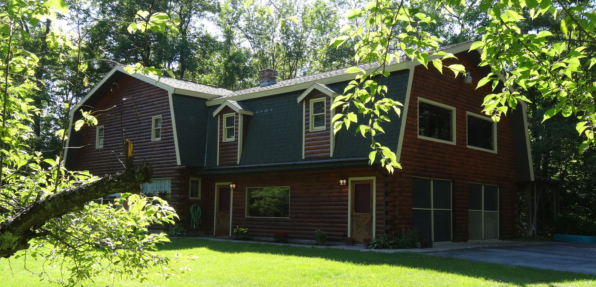 Une cabane en rondins à deux étages, dotée d’un porche à l’avant, d’un garage et d’une pelouse bien entretenue.