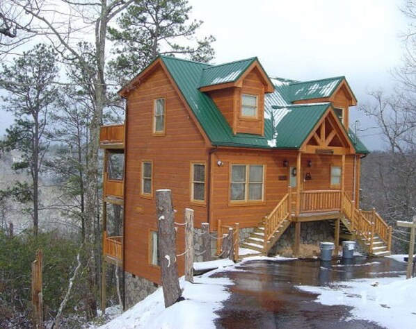 A wooden cabin with a green roof, a front porch, and a staircase leading to the entrance. - Secluded, Privacy, Mountain View, Sunset, 3D Movies, Hot Tub, Hammock + Game Rm (Sevierville)